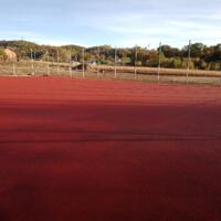 Wyrównany plac o czerwonej ceglanej nawierzchni ogrodzony siatką