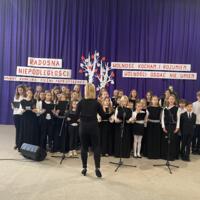 Sala gimnastyczna udekorowana fioletowymi zasłonami oraz napisami RADOSNA NIEPODLEGŁOŚCI gminny konkurs pieśni patriotycznych oraz Wolność kocham i rozumiem - wolności oddać nie umiem, zdjęcia występów konkursowych, wójta dyrektora szkoły, nauczycieli itp...