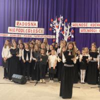 Sala gimnastyczna udekorowana fioletowymi zasłonami oraz napisami RADOSNA NIEPODLEGŁOŚCI gminny konkurs pieśni patriotycznych oraz Wolność kocham i rozumiem - wolności oddać nie umiem, zdjęcia występów konkursowych, wójta dyrektora szkoły, nauczycieli itp...
