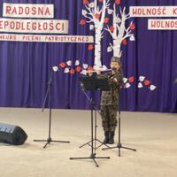 Sala gimnastyczna udekorowana fioletowymi zasłonami oraz napisami RADOSNA NIEPODLEGŁOŚCI gminny konkurs pieśni patriotycznych oraz Wolność kocham i rozumiem - wolności oddać nie umiem, zdjęcia występów konkursowych, wójta dyrektora szkoły, nauczycieli itp...