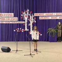 Sala gimnastyczna udekorowana fioletowymi zasłonami oraz napisami RADOSNA NIEPODLEGŁOŚCI gminny konkurs pieśni patriotycznych oraz Wolność kocham i rozumiem - wolności oddać nie umiem, zdjęcia występów konkursowych, wójta dyrektora szkoły, nauczycieli itp...