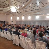 Bal seniora - przy stołach na których znajduje się poczęstunek i napoje siedzą seniorzy - sala jest elegancko przystrojona, niektórzy tańczą