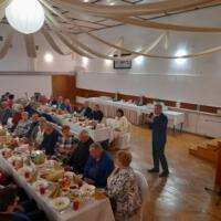 Bal seniora - przy stołach na których znajduje się poczęstunek i napoje siedzą seniorzy - sala jest elegancko przystrojona, niektórzy tańczą