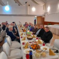Bal seniora - przy stołach na których znajduje się poczęstunek i napoje siedzą seniorzy - sala jest elegancko przystrojona, niektórzy tańczą