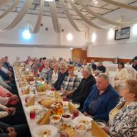 Bal seniora - przy stołach na których znajduje się poczęstunek i napoje siedzą seniorzy - sala jest elegancko przystrojona, niektórzy tańczą