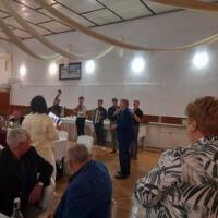 Bal seniora - przy stołach na których znajduje się poczęstunek i napoje siedzą seniorzy - sala jest elegancko przystrojona, niektórzy tańczą