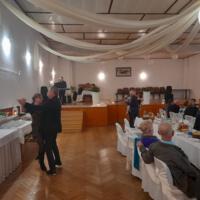 Bal seniora - przy stołach na których znajduje się poczęstunek i napoje siedzą seniorzy - sala jest elegancko przystrojona, niektórzy tańczą