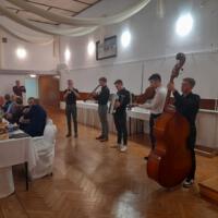 Bal seniora - przy stołach na których znajduje się poczęstunek i napoje siedzą seniorzy - sala jest elegancko przystrojona, niektórzy tańczą