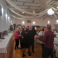 Bal seniora - przy stołach na których znajduje się poczęstunek i napoje siedzą seniorzy - sala jest elegancko przystrojona, niektórzy tańczą