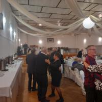 Bal seniora - przy stołach na których znajduje się poczęstunek i napoje siedzą seniorzy - sala jest elegancko przystrojona, niektórzy tańczą