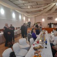Bal seniora - przy stołach na których znajduje się poczęstunek i napoje siedzą seniorzy - sala jest elegancko przystrojona, niektórzy tańczą
