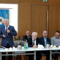 W sali przy stołach siedzi kilkanaście osób, wśród nich starosta powiatu nowosądeckiego, który stoi, na stołach napoje, czajniki i filiżanki, na ścianie sztandar powiatu nowosądeckiego,