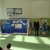 Na sali gimnastycznej obok tablic z napisem Mistrzostwa Gminy Chełmiec stoją Przewodniczący komisji kultury Andrzej Tyrkiel, wójt gminy oraz dyrektorka szkoły, dyrektorka trzyma mikrofon