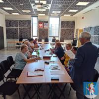 Spotkanie Gminnej Rady Seniorów, osoby siedzą na sali konferencyjnej za stołami, na stołach dokumenty, filiżanki z napojami, 