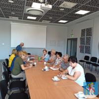 Spotkanie Gminnej Rady Seniorów, osoby siedzą na sali konferencyjnej za stołami, na stołach dokumenty, filiżanki z napojami, 