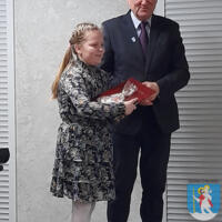 Wójt wręcza dyplom i książkę młodej uczestniczce przeglądu