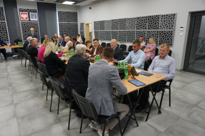 Sesja Rady Gminy Chełmiec - radni siedzą przy centralnie ułożonym stole, na dalszym planie ztół prezydialny, przy stole stoi przewodniczący rady gminy Wiesław Szołdrowski